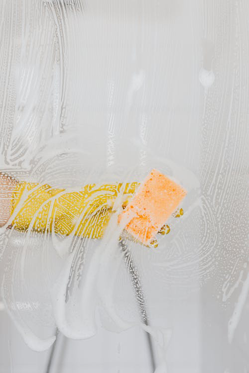  A cleaning maid scrubbing the walls of the shower closet while wearing yellow gloves. 